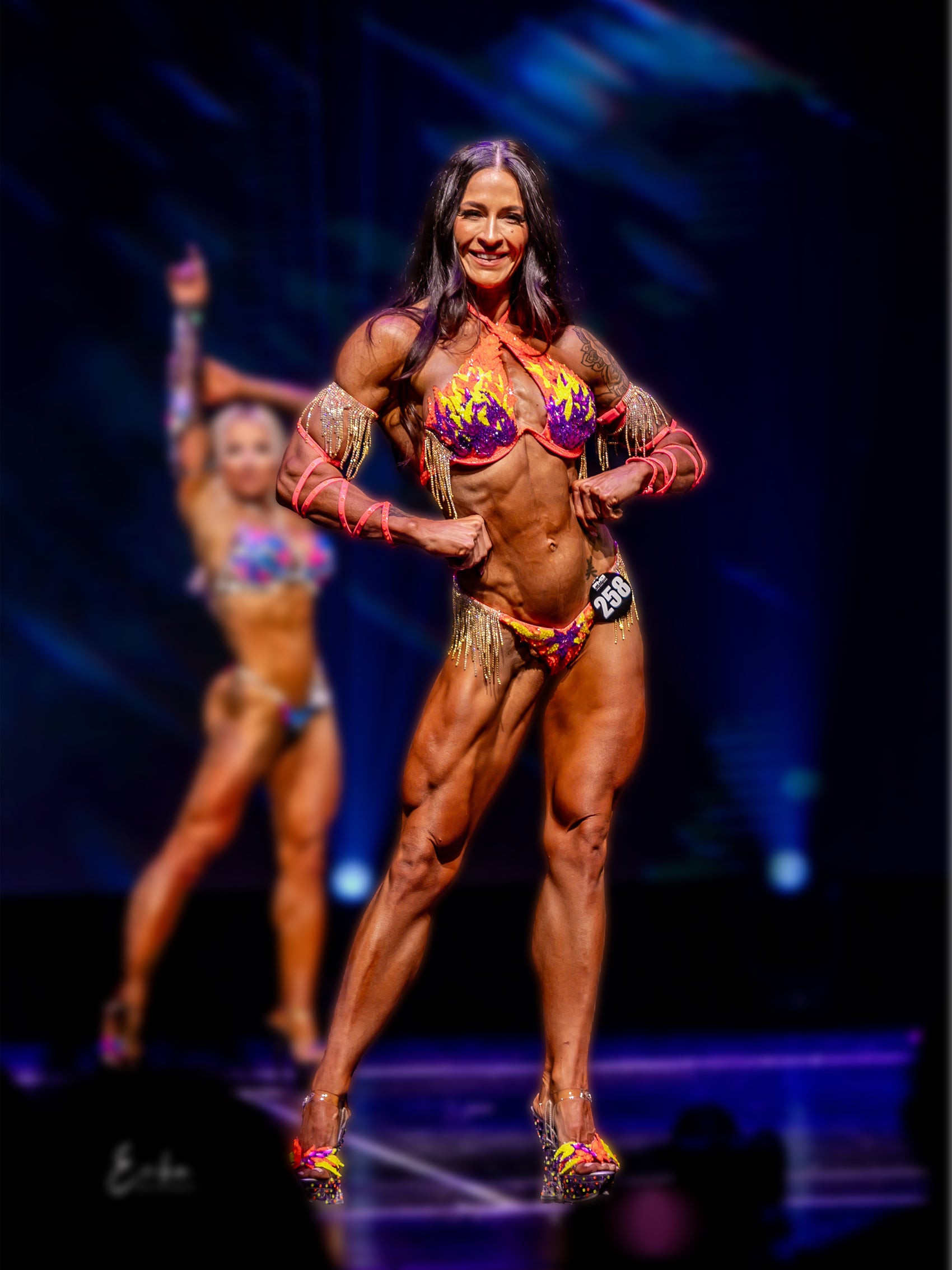 Fitness competitor in a colourful outfit on a stage with a dark background